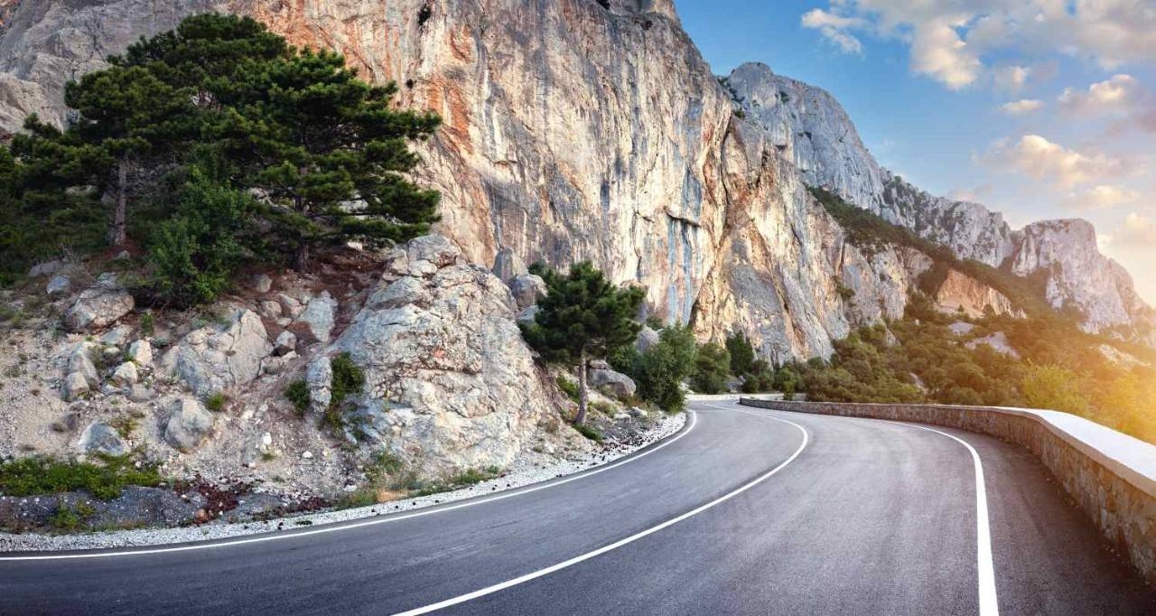 Carretera al borde de una montaña rocosa a la izquierda. Con un árbol en la roca y puesta del sol a la izquierda
